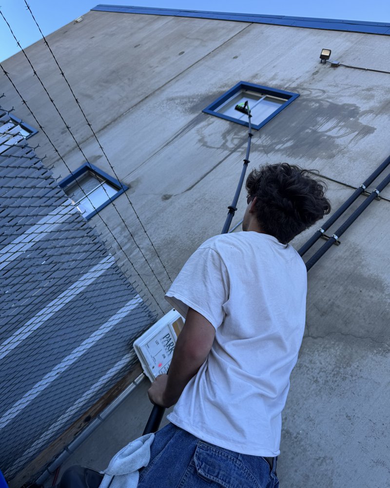 Kai washing an upper-story commercial window with a water-fed pole